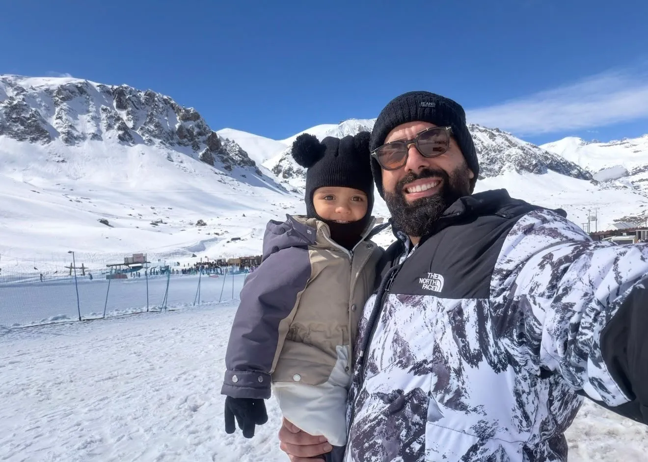 Pai com o filho na neve, com montanhas ao fundo
